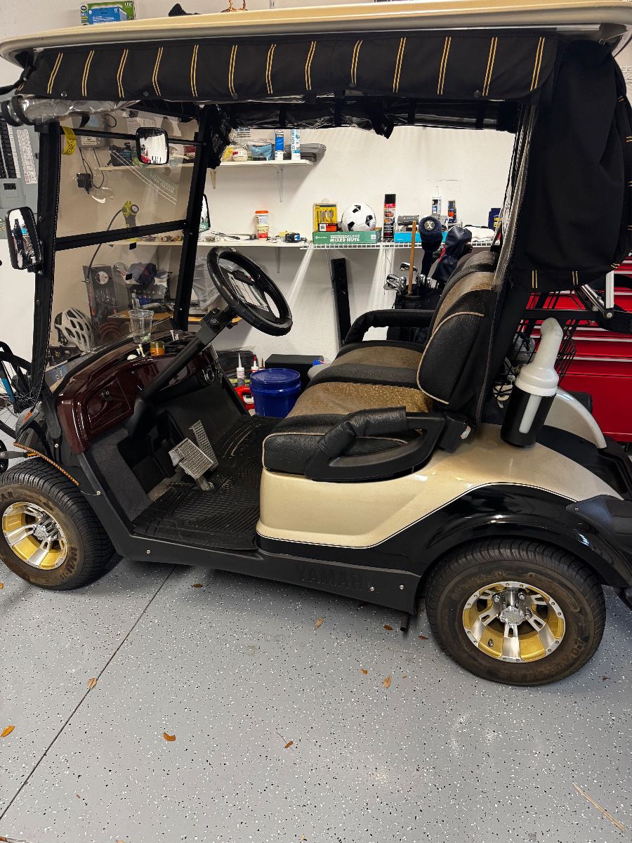 Yamaha gas-powered golf cart featuring custom two-tone seating, upgraded wheels, windshield, overhead storage, and premium canopy enclosure. Clean well-maintained condition with comfortable seating and stylish Village-ready appearance. Great for neighborhood cruising, recreation, or everyday community transportation.