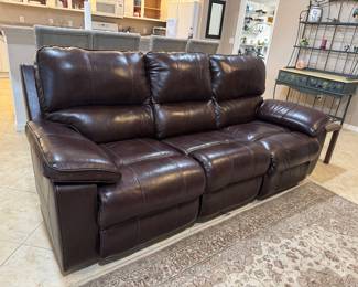 Contemporary dark brown leather wall-hugger power reclining sofa with plush seating, oversized padded arms, and built-in USB charging port controls. Features smooth power recline functionality, rich genuine leather upholstery, and space-saving wall-hugger design ideal for smaller rooms or condos. Exceptional comfort with clean modern styling perfect for family room, media room, or everyday living.