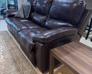 Contemporary dark brown leather wall-hugger power reclining sofa with plush seating, oversized padded arms, and built-in USB charging port controls. Features smooth power recline functionality, rich genuine leather upholstery, and space-saving wall-hugger design ideal for smaller rooms or condos. Exceptional comfort with clean modern styling perfect for family room, media room, or everyday living.