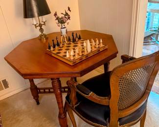 octagonal game or accent table with unique lattice trim below. Wooden chess set and candle stick lamp with vintage black leather seated woven back arm chair.