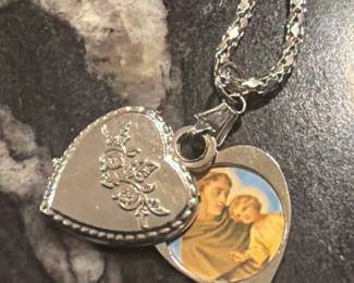 Heart shaped locket necklace with engraved detail and small religious charm inside. Sweet vintage keepsake piece with sentimental appeal,