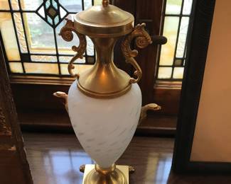 Ornate Decorative Urn with Cherub Finial Elegant, vintage‑style decorative urn featuring a frosted white body with subtle etched detailing and rich gold‑tone accents. The piece includes beautifully sculpted scroll handles, an ornate square base with claw‑style feet, and a highly detailed cherub finial on the lid. A striking display piece with classic European influence, perfect for a mantel, entry table, or formal living space.  Condition: