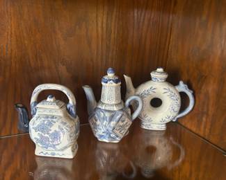 Set of Three Blue‑and‑White Decorative Ceramic Teapots Charming set of three blue‑and‑white ceramic teapots, each with its own unique shape and hand‑painted design. The pieces feature floral and geometric patterns in classic cobalt tones, giving them a timeless, collectible appeal.  Left Teapot: Square‑bodied with curved handle and delicate floral motifs.  Center Teapot: Hexagonal form with intricate geometric and botanical detailing.  Right Teapot: Circular sculptural body with an open center and soft leaf‑and‑flower patterns.  These teapots make a beautiful display set for a china cabinet, shelf, or kitchen décor.  Condition: Excellent; no visible chips or cracks. Includes: All three teapots as shown.
