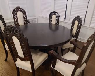 Elegant Carved Dining Table with Six Upholstered Armchairs Beautiful round dark‑wood dining table paired with six ornate carved chairs, each featuring gracefully detailed backs, sculpted arms, and light upholstered seats and panels. The craftsmanship is exceptional — rich wood tones, intricate carving, and a classic silhouette that brings warmth and sophistication to any dining room.  The set seats six comfortably and creates an inviting, traditional atmosphere perfect for gatherings, holidays, or everyday dining.  Includes:  Round wooden dining table  Six matching carved armchairs with upholstered seats and backs  Condition: Excellent; sturdy, well cared for, and visually striking.