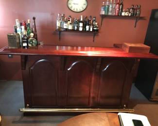 Free-standing.  Solid Wood Home Bar with Brass Foot Rail Handsome solid wood home wet bar featuring a rich, polished finish and three paneled front sections that give it a classic, upscale look. The bar includes a brass foot rail, adding both comfort and a traditional pub‑style touch. Its generous countertop provides plenty of space for serving, mixing, or display.  Perfect for an entertainment room, den, or basement lounge, this piece brings warmth, character, and functionality to any hosting space.  Condition: Very good; clean, sturdy, and well cared for.