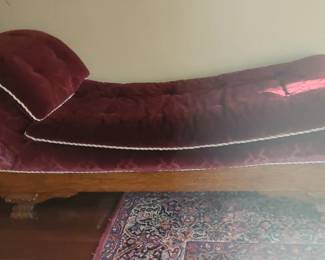 Vintage Burgundy Velvet Chaise Lounge – 75" x 26" x 20" Elegant vintage chaise lounge upholstered in rich burgundy velvet with crisp white trim outlining the curves. Features a classic fainting‑sofa silhouette with a raised, gendntly curved backrest on one side and a long, cushioned seat for lounging. The wooden base a carved legs add warmth and traditional charm.  This piece brings a touch of Victorian‑inspired style and makes a beautiful statement in a bedroom, sitting room, or reading nook. Condition: Very good; upholstery and frame present well.