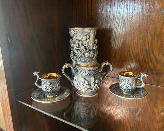 Decorative Porcelain Dragon‑Handle Tea Set – Teapot, Cups & Saucers Striking porcelain tea set featuring an intricately sculpted teapot with two matching cups and saucers. Each piece is richly detailed with raised relief scenes and ornate classical‑style figures. The exterior has a soft gray‑blue finish, beautifully contrasted by gilded interiors and rims that add a luxurious touch.  The standout feature is the dragon‑shaped handles on the cups—an elegant, artistic detail that makes this set especially collectible. The craftsmanship is exceptional, with deep texture, dimensional sculpting, and fine gold accents throughout.  A stunning display set for collectors of decorative porcelain or anyone who appreciates unique, sculptural ceramics.  Includes:  Teapot  Two cups  Two saucers  Condition: Excellent; no visible chips or cracks, gilding bright and intact.