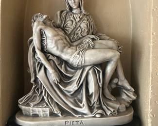 Pietà Sculpture – Mary Holding Jesus Beautiful Pietà sculpture depicting the Virgin Mary cradling the body of Jesus with finely rendered drapery and expressive detail. The piece is crafted in a metallic stone‑like finish that highlights the folds, contours, and emotional depth of the scene. It rests on a black base inscribed with “PIETÀ,” giving it a classic, museum‑style presentation.  A meaningful devotional piece and a striking addition to any religious art collection.  Condition: