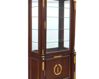 1088 An Empire style gilt bronze mounted mahogany vitrine Early 20th century Mounted with gilt-bronze Egyptian revival motifs including masks, medallions, and palmettes, with an upper glazed locking door revealing two adjustable glass shelves, above a cabinet door opening to reveal three document drawers above an open compartment 83" H x 39" W x 21.5" D Estimate: $2,500 - $3,500