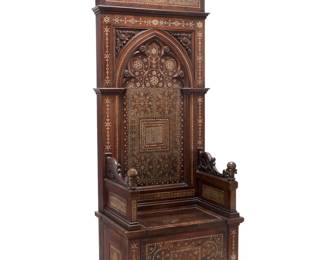 1375 A Gothic Revival bone inlaid mixed wood throne chair 19th century With denticulated pediment above an archway seatback carved with foliate motifs and inlaid with bone, forming geometric designs, the seat a hinged lid for an open compartment, the armrest supports, seat front, and sides conformingly inlaid 81.75" H x 30" W x 21.5" D Estimate: $1,000 - $2,000