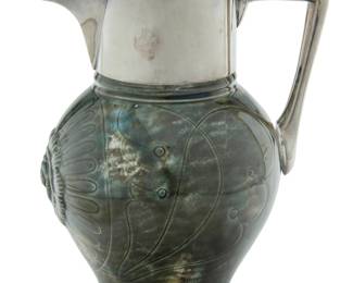 1105 A Hukin & Heath electroplated silver and Wedgwood majolica pitcher Early 20th century, the mounts possibly designed by Christopher Dresser (1834-1904) The metal marked for Hukin & Heath; the ceramic impressed: WEDGWOOD M BCK [for 1925] The globular body with hare's fur glaze, a mask of Elizabeth I in relief below the spout 7.5" H x 5.625" W x 4.625" D Estimate: $500 - $700