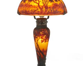 1116 A Daum cameo glass landscape table lamp Early 20th Century Signed: Daum Nancy [Croix de Lorraine] With two lights, one illuminating the base, the base and shade each decorated with a landscape scene, electrified Overall: 16.17" H x 9" Dia. Estimate: $1,000 - $1,500