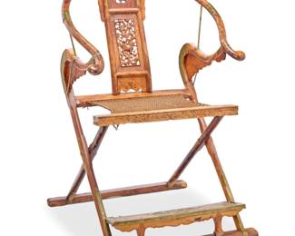 1154 A Chinese elmwood folding chair 20th century With horseshoe crest rail and carved wood splat depicting a chilong figure among clouds, above a folding X-frame with corded seat and footrest, with brass joints and decorative mounts 43.75" H x 29.5" W x 30.5" D Estimate: $800 - $1,200