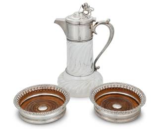 1239 An English silver plated and glass claret jug and two coasters Late 19th century Lid impressed: MAPPIN&WEBB / 884-7; each coaster with impressed raven at center The Mappin & Webb silver plate mounted molded glass claret jug with finial in the form of a lion and shield inscribed 'SCIO OUI CONFIDO'; the pair of Sheffield plate wine coasters with wood bases 3 Pieces Jug: 11.25" H x 6.75" W x 5.75" D; Each coaster: 1.875" H x 6.125" Dia. Estimate: $300 - $500