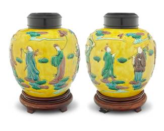 1009 A pair of Chinese yellow ground ceramic ginger jars Qing Dynasty (1644-1912) or later Each bearing Wang Bingrong maker's mark in glazed relief Decorated with molded figures in low relief, with carved wood bases and pierced lids 2 pieces Each jar without lid: 8.5" H x 8.5" Dia.; Each overall: 11.375" H Estimate: $1,000 - $1,500
