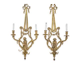 1315 A pair of French bronze wall sconces 20th century Each with bow and ribbon above central trumpeter putto, garlands, and a pinecone drop finial, issuing two lights with faux candle fixtures, electrified 2 pieces Each: 40.5" H x 16.25" W x 7.75" D Estimate: $1,000 - $1,500