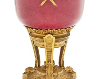 1195 A French gilt bronze and porcelain centerpiece 19th century With pierced laurel wreath rim above a raspberry glazed porcelain bowl, raised on a tripod base with lion paw feet and central flame finial 13.375" H x 10.5" Dia. Estimate: $800 - $1,200