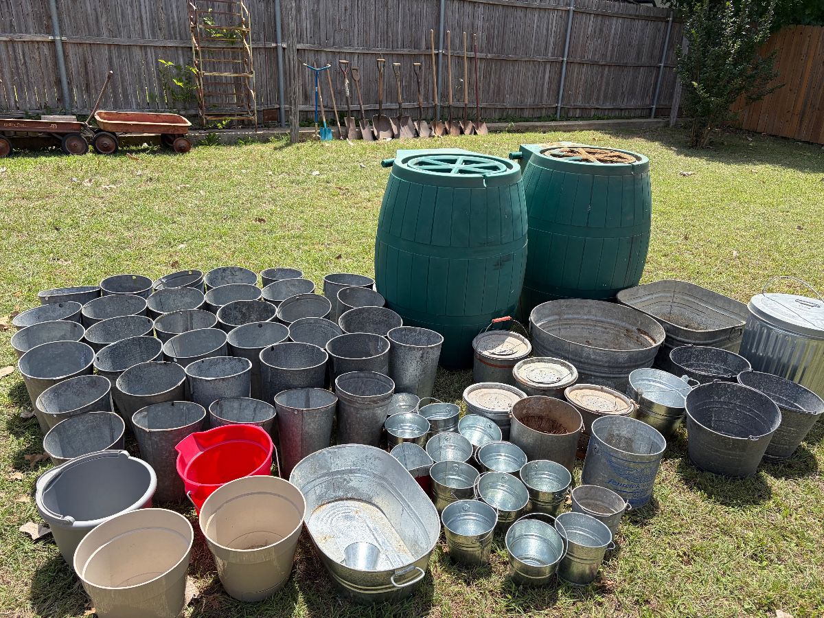 Backyard filled with galvanized steel buckets in all sizes. Four 75 gallon rain barrels