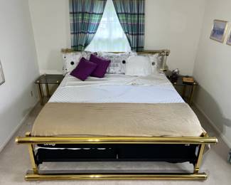 A luxurious MCM bedroom anchor piece consisting of a solid brass thick tubular king size bed frame flanked perfectly by a pair of matching smoked glass-top nightstands on polished brass pillar legs. (Mattress and box spring set sold separately)