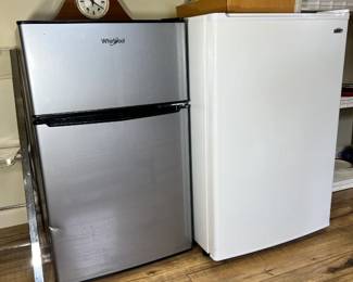 A modern stainless steel/black Whirlpool mini-fridge with a separate top freezer door, sitting next to a white Summit compact freezer unit.