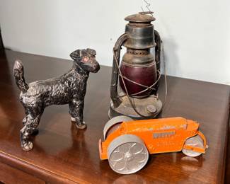 A vintage walnut office desk holding an antique iron Scottie dog doorstop, a Dietz railroad lantern, and a toy steamroller.