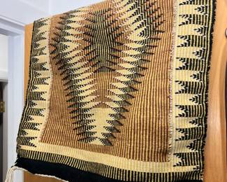 A small vintage Native American woven wool rug draped over a wooden door, featuring a striking geometric tribal pattern in rich earth tones.