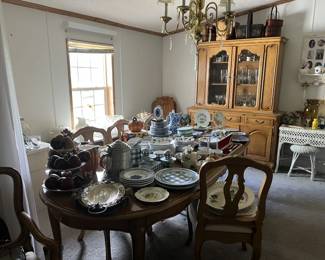A table covered in matching sets of china and dishware. There are also collectible plates, and a three-tiered dessert plate covered in replica wooden fruit.