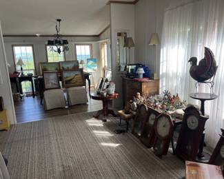A glimpse between the first two room in the estate sales. There is a variety of furniture, a collection of small animal figurines, a collection of grandfather clocks, and a collection of original paintings.