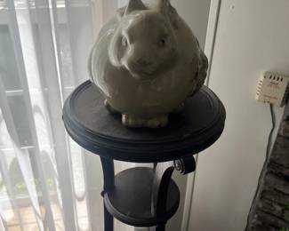 Rotund ceramic bunny statue, sitting atop a wooden pedestal.