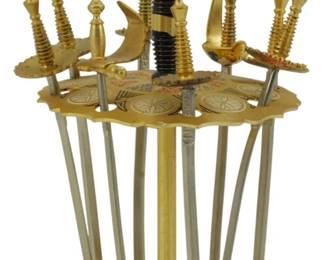 567 - Vtg Toledo Cocktail Pick Set w/ Stand 4" (Description): Vintage Toledo cocktail pick set featuring miniature decorative swords with ornate gilt handles in various styles including scimitars and rapiers. The picks have stainless steel blades and rest in a coordinating gilt metal stand with damascene-styledecoration and scalloped edges. The stand measures 4 inches tall and holds approximately twelve picks. A charming barware accessory from Spain.