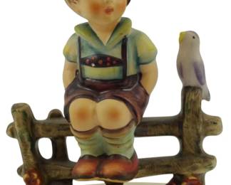 561 - Hummel Wayside Harmony 1933 Figure 4.5" (Description): Hummel "Wayside Harmony" figurine from 1933. This charming piece depicts a young Bavarian boy in traditional lederhosen sitting on a rustic wooden fence with a small bird perched beside him. The boy wears a green Alpine hat with a feather, a light blue shirt, brown lederhosen, green knee socks, and brown shoes. Delicate hand-painted details include rosy cheeks and small flowers at the base of the fence. Measures 4.5 inches tall.