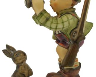 563 - Hummel Good Hunting Figure 5.5" (Description): Hummel "Good Hunting" porcelain figurine depicting a young boy in traditional Bavarian attire with a green plaid shirt and hat, holding binoculars while carrying a rifle on his back. A small brown rabbit sits at his feet on the cream-colored oval bse. Measures 5.5 inches tall.