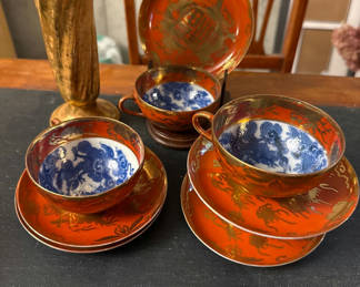 Lot 73: Orange-red porcelain teacups with blue interiors, matching saucers and plate, plus a gold vase