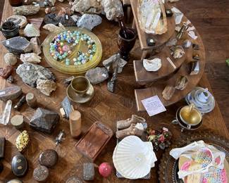 Tabletop treasure mix with rocks, minerals, crystal points, shells, brass pieces, beads, carved boxes, bottles, and small curiosities.