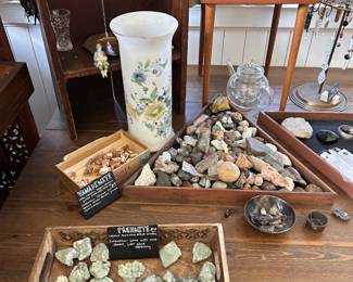 Mineral and rock specimens, labeled stones, floral vase, glass vessel, small figurine, and decorative tabletop pieces.