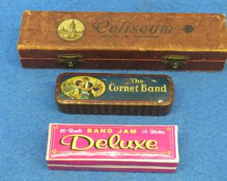 Lot 84. Three empty harmonica boxes: 7 1/2" Coliseum hinged box with metal clasps. Metal 4" hinged The Cornet band box. 3 3/4" hinged Band Jam Deluxe box.