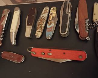 Vintage pocket knife and multi-tool collection featuring folding knives, corkscrew utility knives, advertising knives, and classic camping/outdoor styles
