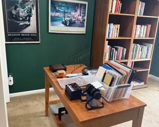 Wood desk, pictures, wood bookshelves and lots of books. Office supplies