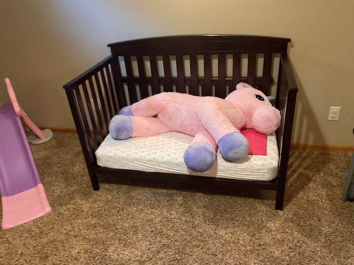 Very large, plush stuffed unicorn on a toddler size bench bed