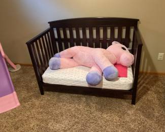Very large, plush stuffed unicorn on a toddler size bench bed