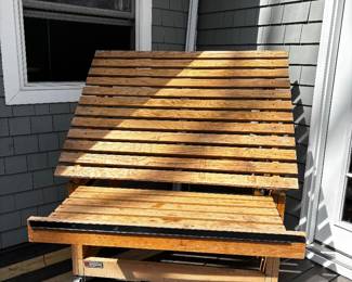 A portable wooden slatted tilt-top product display table with wheels. 