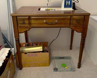There is a Singer Touch & Sew II sewing machine and sewing cabinet in this photo. Over to the left is a partial view of an exercise machine, which sort of fits with the glass-top scale shown here.