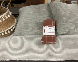 Lot 130: Woven throw blanket, straw basket with tassels, grey cushions, and tassel rug