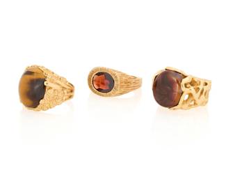 1113 A Group of Three 14K Gold Rings Featuring organic designs centering an oval garnet, tiger's eye cabochon and Mexican fire agate cabochon 3 pieces Sizes: 8 3/4 and 9 45.9 grams gross Estimate: $2,800 - $3,500