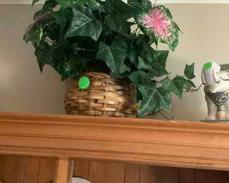 A flower arrangement in basket on top of China cabinet. Has two ceramic elephants on each side.
