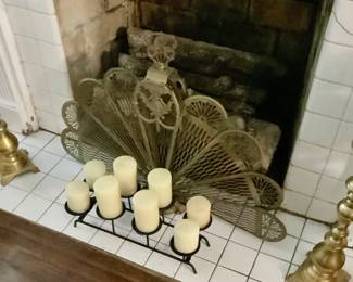 Brass fire screen, sitting in front of that is a black candle holder with 8 candles.