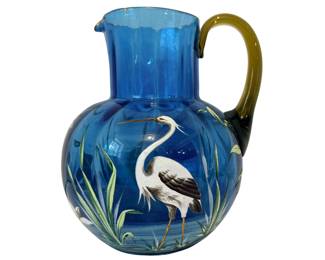  Antique Victorian Enameled Art Glass Water Pitcher.   Antique Victorian enameled art glass water pitcher, roughly 7.5 inches tall, dating from the late 19th century (circa 1880–1900). It is crafted from a vibrant translucent mid-blue blown glass. The amber/olive-green colored handle is explicitly an applied glass handle, fused to the body after the main pitcher vessel was blown.