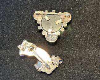 Reverse views of signed William Spratling silver and onyx brooch, and an unsigned Spratling silver hand holding carved amethyst flower brooch