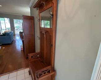 Charming antique entryway piece featuring a built-in bench, storage compartment, mirror, and multiple coat hooks. A beautiful and functional entryway piece with  warm wood character.