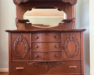 Beautiful antique solid oak hutch featuring intricate carved details, an elegant oval mirror, and rich wood grain throughout. Includes three center drawers, two side cabinets, and a large lower drawer for ample storage.